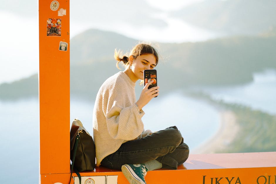 リキヤ展望台に座り、携帯電話で穏やかな風景を撮影している若い女性。