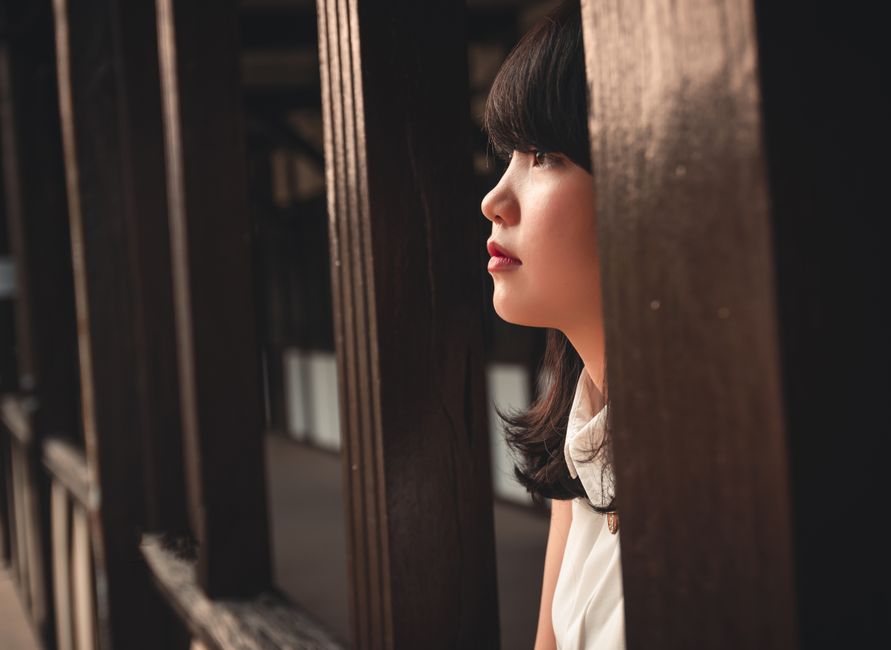 ベトナム、コントゥムの屋外で木の格子越しに見つめる若い女性のポートレート。