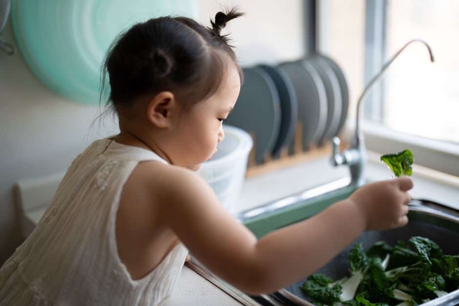 子供がシンクで新鮮な野菜を洗い、健康的な習慣を示しています。