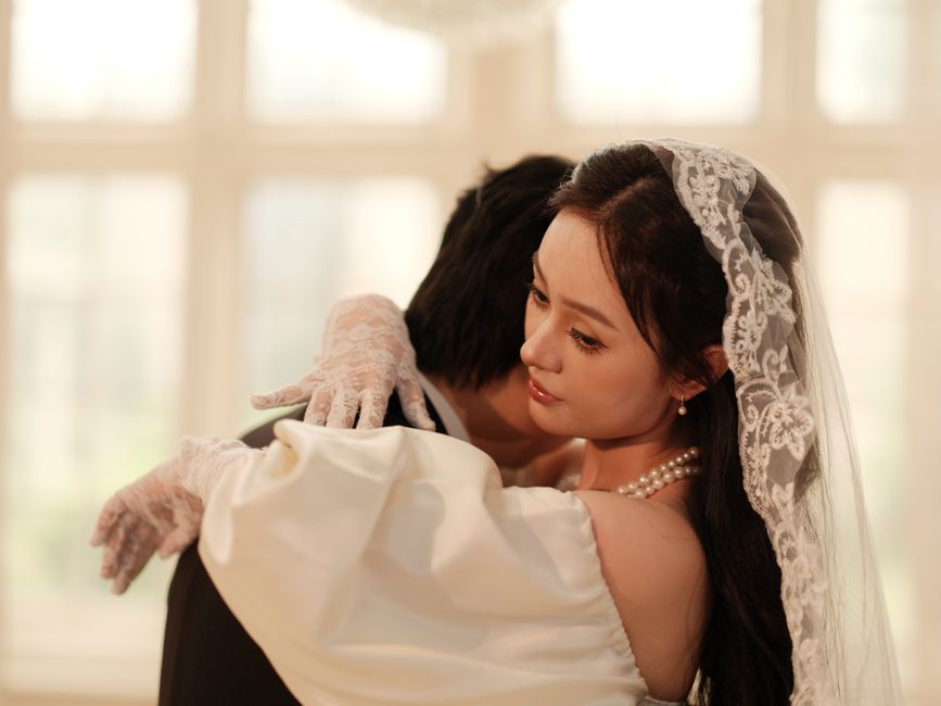 優雅なレースのベールをまとった花嫁が、ロマンチックな屋内結婚式会場で花婿を抱きしめている。