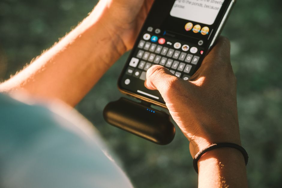 屋外でモバイルバッテリーにつないだスマートフォンを操作する手元