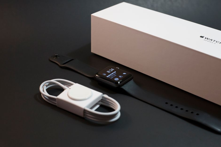 現代的なスマートウォッチと充電器が、暗い表面の上にそのパッケージと並んで優雅に展示されています。