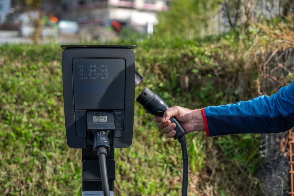 充電ケーブルを持った手がある屋外の電気自動車充電ステーション。