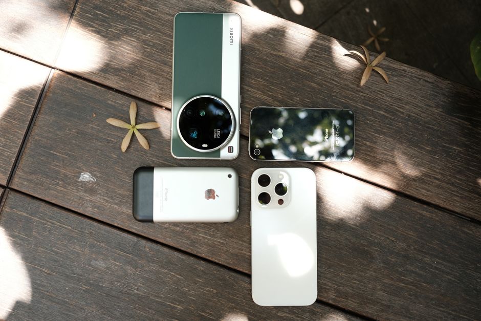 木漏れ日の当たる屋外の木製テーブルの上に、様々なスマートフォンが並べられている。