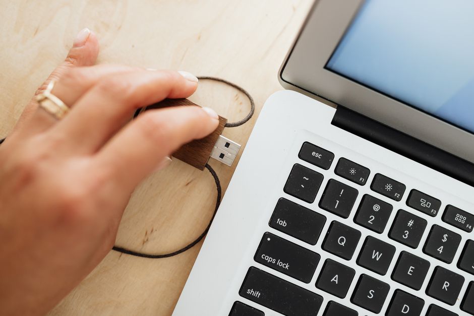 木製のUSBを木製のテーブルの上のラップトップに挿入している手。