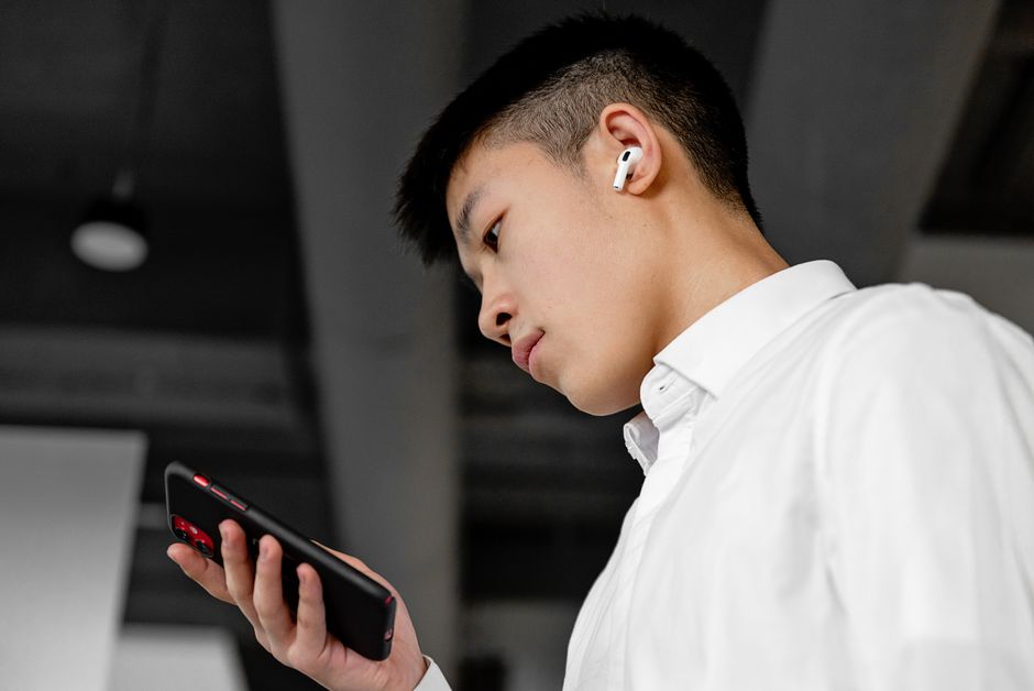 ワイヤレスイヤフォンを着用し、室内でスマートフォンを使っている若い男性の横からの視点。