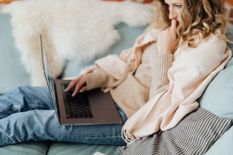 電気ひざ掛けを掛けてソファでノートPC作業をする女性