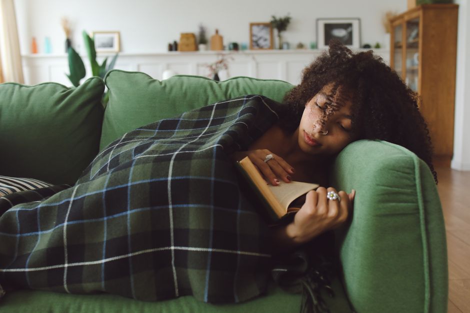 ブランケットにくるまってソファで読書をする女性 電気ひざ掛けで足元の冷え対策